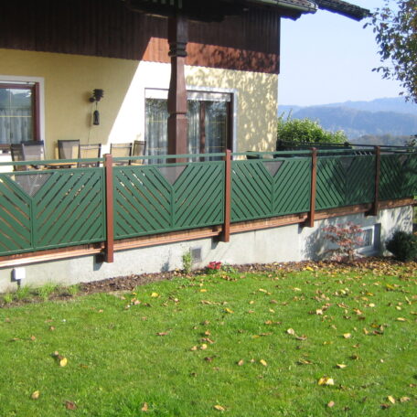Grüner Metallzaun vor Einfamilienhaus mit Garten, im Hintergrund Berge und Landschaft. HANSEL.kraus metalltechnik gmbh