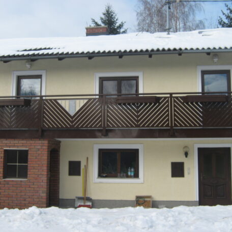 Zweistöckiges Haus mit Balkon, Schneebedecktes Dach, verschneiter Vorgarten, vier sichtbare Fenster. de HANSEL.kraus metalltechnik gmbh