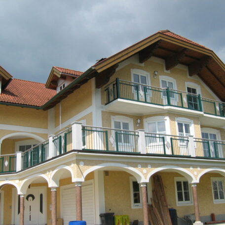 Großes gelbes Einfamilienhaus mit Balkon und rotem Satteldach, bewölkter Himmel darüber. de HANSEL.kraus metalltechnik gmbh