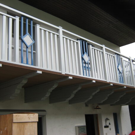 Balkon mit weißem Geländer und blauen Holzornamenten an einem Wohnhaus. HANSEL.kraus metalltechnik gmbh