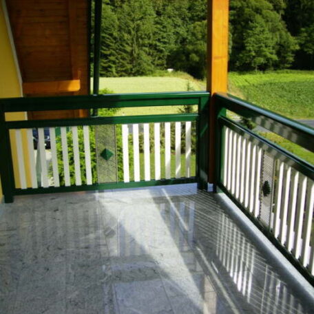Sonniger Balkon mit Holzgeländer, Blick auf grüne Wiese und bewaldete Landschaft. HANSEL.kraus metalltechnik gmbh