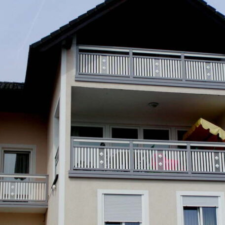 Mehrstöckiges Haus mit weißen Balkonen und Holzdach im Vordergrund. HANSEL.kraus metalltechnik gmbh