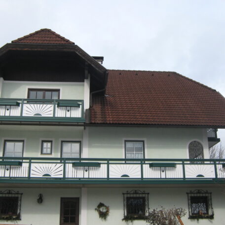 Zweistöckiges Haus mit braunem Dach, weißen Wänden und grünen Balkonen, im Landhausstil. HANSEL.kraus metalltechnik gmbh