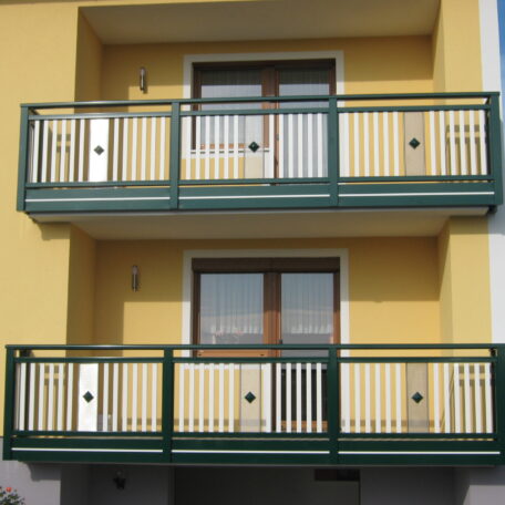 Zwei grüne Balkone an gelber Hausfassade mit weißen Türen, frontal fotografiert. HANSEL.kraus metalltechnik gmbh