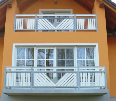 Zwei Balkone mit weißen, geometrischen Geländern an orange gestrichener Hausfassade, moderne Architektur. HANSEL.kraus metalltechnik gmbh