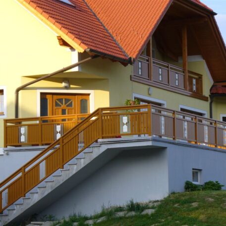 Gelbes Einfamilienhaus mit rotem Dach, breiter Rampe und Holzgeländer am Eingang. HANSEL.kraus metalltechnik gmbh