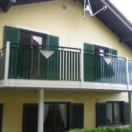 Gelbes Haus mit grünem Balkon und Fensterläden, zwei Fenster und Balkon im Obergeschoss. HANSEL.kraus metalltechnik gmbh