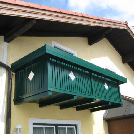 Grüner Sichtschutz für Balkon an gelber Hauswand unter Satteldach, blauer Himmel. HANSEL.kraus metalltechnik gmbh