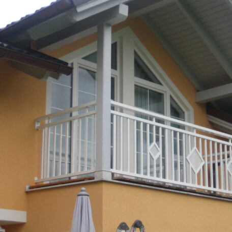 Moderner Balkon mit weißem Geländer und Dreiecksfenstern an gelber Hausfassade. HANSEL.kraus metalltechnik gmbh
