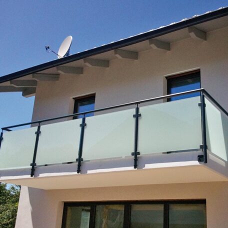 Moderner Balkon mit Glasgeländer an einem weißen Einfamilienhaus unter blauem Himmel. HANSEL.kraus metalltechnik gmbh