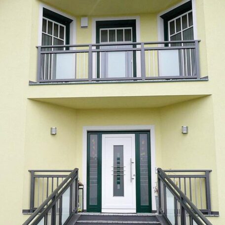 Zweistöckiges gelbes Haus mit weißer Haustür, Balkon und symmetrischem Treppenaufgang. HANSEL.kraus metalltechnik gmbh