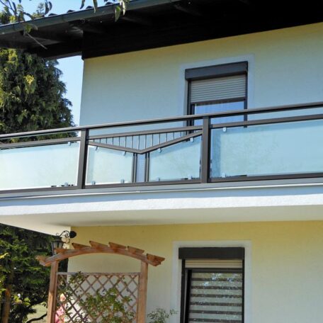 Zweistöckiges Wohnhaus mit Balkon, Glasgeländer und kleiner Holzbogen im Garten. HANSEL.kraus metalltechnik gmbh