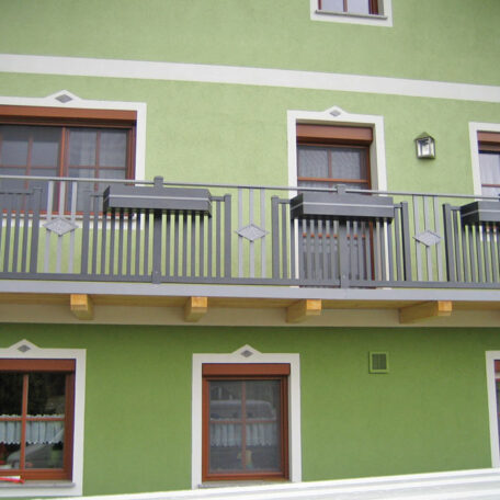 Grüne Hausfassade mit Balkon, weißen Zierstreifen und braunen Fensterrahmen auf Imagefilm-Produktion Landingpage. HANSEL.kraus metalltechnik gmbh