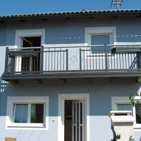 Zweistöckiges, blaues Wohnhaus mit Balkon und weißen Fenstern, aufgenommen bei Tageslicht. HANSEL.kraus metalltechnik gmbh