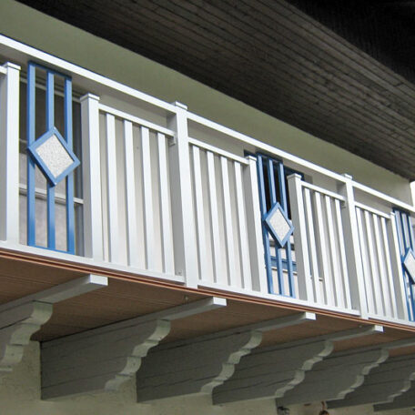 Ein langer Holzbalkon mit weißen und blauen Ziergeländern an einem Gebäude. HANSEL.kraus metalltechnik gmbh