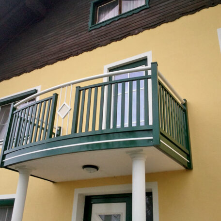 Grünes Balkongeländer an gelber Hausfassade mit weißer Tür und zwei Fenstern. HANSEL.kraus metalltechnik gmbh