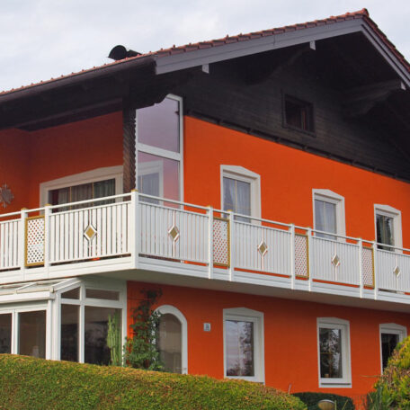 Modernes Einfamilienhaus mit orangefarbener Fassade, weißem Balkon und gepflegtem Garten, Außenansicht. HANSEL.kraus metalltechnik gmbh