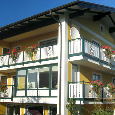 Gelbes Mehrfamilienhaus mit weißen Balkonen und Blumenkästen, sonniger Tag, blauer Himmel. HANSEL.kraus metalltechnik gmbh