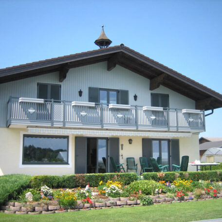 Einfamilienhaus mit Balkon, gepflegtem Vorgarten und bunten Blumen bei sonnigem Wetter. de HANSEL.kraus metalltechnik gmbh