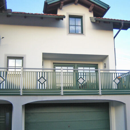 Zwei grüne Garagentore und Balkon mit Metallgeländer an einem hellen Einfamilienhaus. HANSEL.kraus metalltechnik gmbh