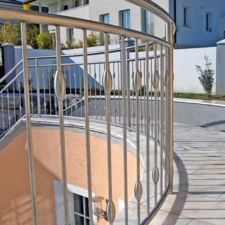 Geschwungenes Edelstahlgeländer auf moderner Außentreppe vor einem hellen Wohnhaus. HANSEL.kraus metalltechnik gmbh