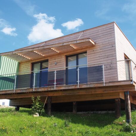 Modernes Containerhaus mit Holzverkleidung und großer Terrasse auf einer grünen Wiese. HANSEL.kraus metalltechnik gmbh