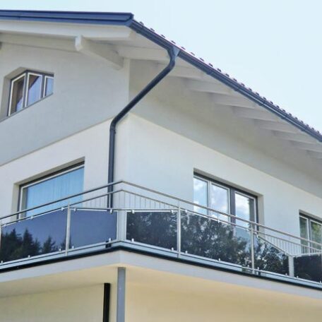 Modernes weißes Einfamilienhaus mit großem Balkon und Glasgeländer, blaue Fensterrahmen. HANSEL.kraus metalltechnik gmbh