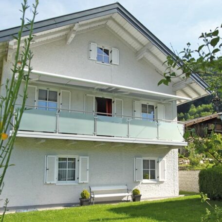 Zweistöckiges Einfamilienhaus mit Balkon, weißen Fensterläden und gepflegtem Garten an sonnigem Tag. HANSEL.kraus metalltechnik gmbh