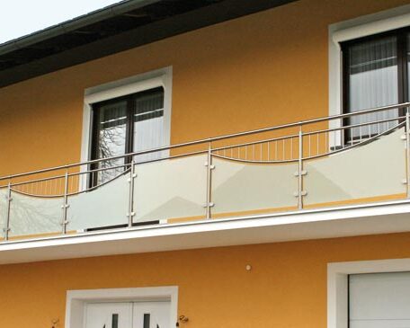 Zweistöckiges Haus mit gelber Fassade und modernem Glasgeländer am Balkon. HANSEL.kraus metalltechnik gmbh