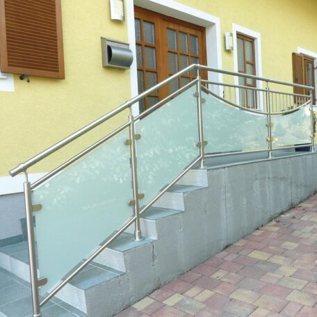 Barrierefreie Rampe mit Edelstahlgeländer und Milchglas vor gelber Hausfassade, Zugang zu Holztür. HANSEL.kraus metalltechnik gmbh