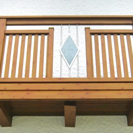 Holzbalkon mit senkrechten Streben und rautenförmigem Glaselement an weißer Hausfassade. HANSEL.kraus metalltechnik gmbh