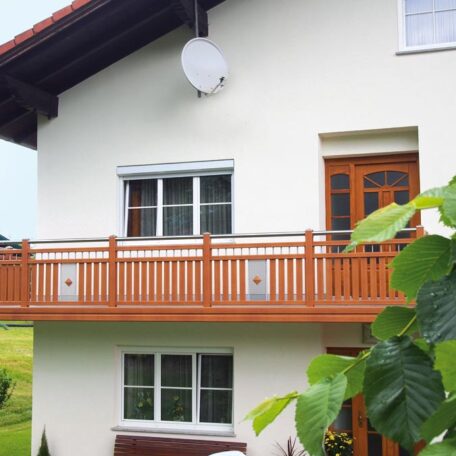 Zweistöckiges Wohnhaus mit Holz-Balkon, weißen Wänden und einer Satellitenschüssel an der Fassade. HANSEL.kraus metalltechnik gmbh