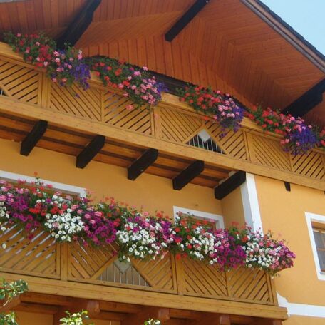 Balkon mit bunten Blumen am gelben Haus, sommerliches Ambiente, sonniger Tag. HANSEL.kraus metalltechnik gmbh