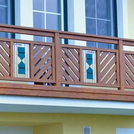 Holzbalkon mit dekorativen Einsätzen vor gelber Hausfassade und großen weißen Fenstern. HANSEL.kraus metalltechnik gmbh