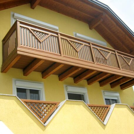 Balkon aus Holz an gelber Hausfassade mit drei Fenstern im Landhausstil. HANSEL.kraus metalltechnik gmbh