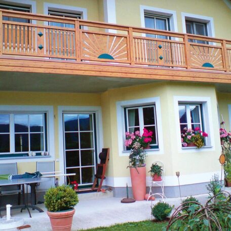 Gelbes Einfamilienhaus mit Holzbalkon, Blumenkästen und kleiner Terrasse im Grünen. HANSEL.kraus metalltechnik gmbh
