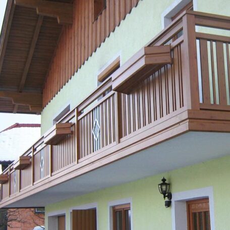 Holzbalkon mit senkrechten Streben an gelber Hausfassade, traditioneller Stil, Tageslicht. HANSEL.kraus metalltechnik gmbh