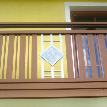 Braunes Balkon-Geländer mit Dekorelement auf gelber Wand, Fenster im Hintergrund. HANSEL.kraus metalltechnik gmbh