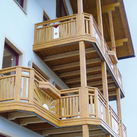 Mehrstöckige Hausfassade mit drei übereinanderliegenden Holzbalkonen und verzierten Geländern. HANSEL.kraus metalltechnik gmbh