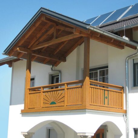 Balkon mit Holzgeländer, weißer Fassade und Solarpanelen auf dem Dach bei Sonnenschein. Sprache: de HANSEL.kraus metalltechnik gmbh