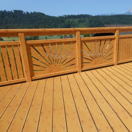 Holzterrasse mit dekorativem Sonnenmuster im Geländer und Ausblick auf grüne Landschaft. HANSEL.kraus metalltechnik gmbh