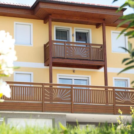 Zweistöckiges, gelbes Haus mit Holzgeländern, Balkon und weißen Fensterläden im Sonnenschein. HANSEL.kraus metalltechnik gmbh