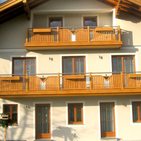 Fassade eines Hauses mit mehreren Holzbalkonen, Fensterfront und Satteldach bei Tageslicht. HANSEL.kraus metalltechnik gmbh