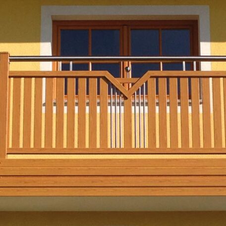Holzbalkon mit senkrechten Streben vor einer Doppeltür, gelbe Hausfassade, sonnig. HANSEL.kraus metalltechnik gmbh