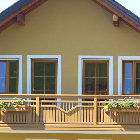 Holzbalkon mit Blumenkästen, drei Fenster, gelbe Fassade, traditionelles Haus in Freiburg. HANSEL.kraus metalltechnik gmbh