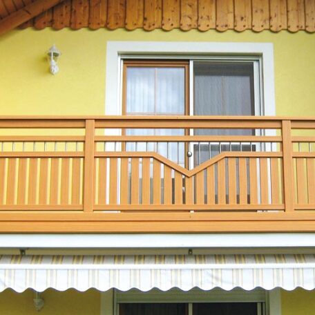 Oberer Holzbalkon mit Geländer vor gelber Hauswand und Glas-Schiebetür, Markise unten. HANSEL.kraus metalltechnik gmbh