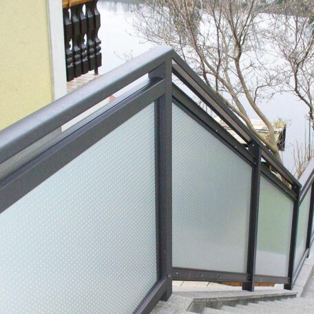 Treppengeländer mit Milchglasfüllung und Metallrahmen neben Haus, Bäume im Hintergrund. HANSEL.kraus metalltechnik gmbh
