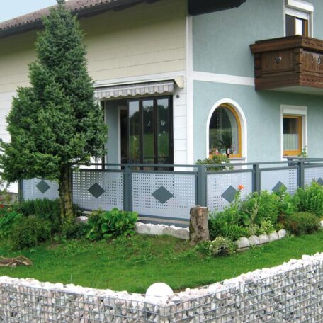 Garten mit dekorativem Metallzaun, gepflegtem Rasen, Sträuchern und modernem Einfamilienhaus im Hintergrund. HANSEL.kraus metalltechnik gmbh