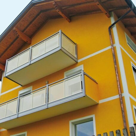 Zwei weiße Balkone an gelber Hausfassade mit Holzdach, modernes Wohngebäude. HANSEL.kraus metalltechnik gmbh
