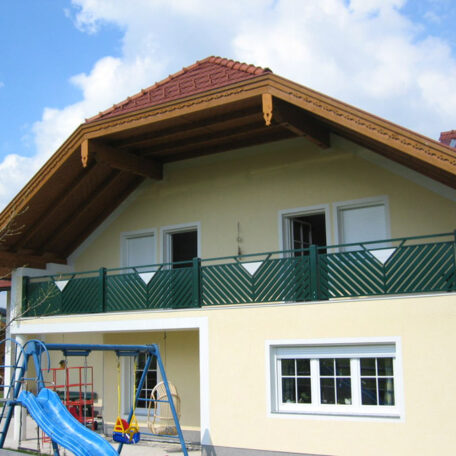 Einfamilienhaus mit grünem Balkon, überdachter Terrasse und Spielplatz im Vordergrund bei Tageslicht. HANSEL.kraus metalltechnik gmbh